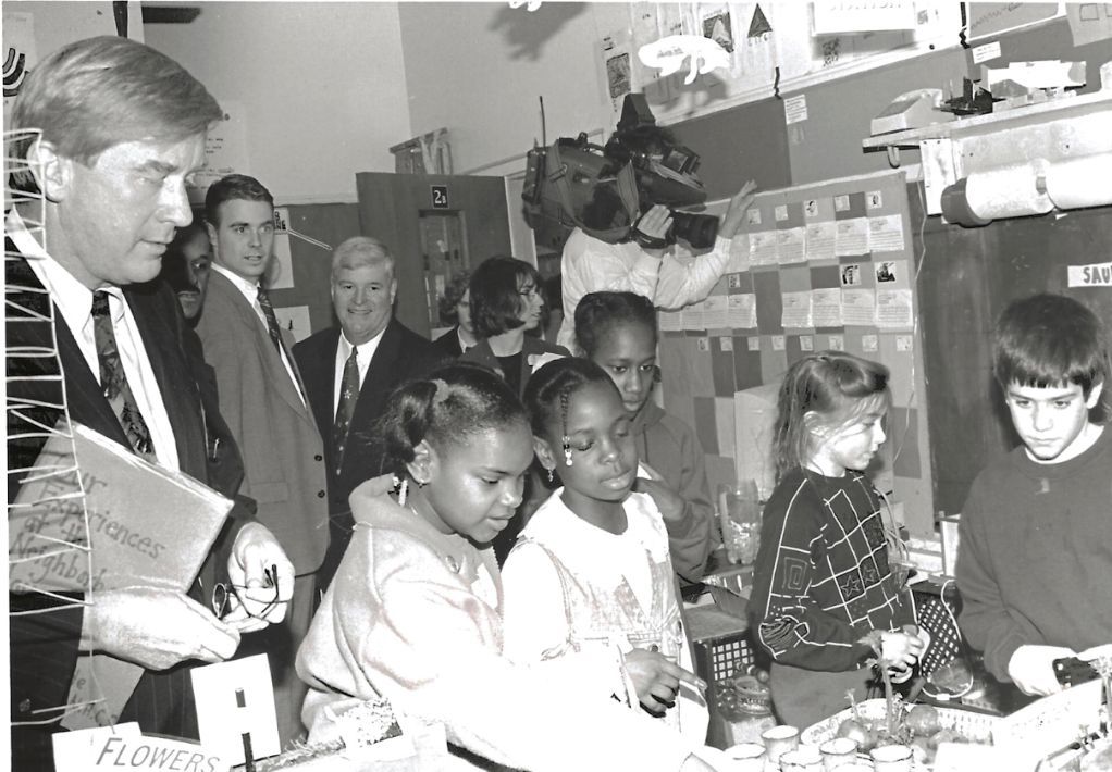 Governor William Weld visiting the Kid Lab at Neighborhood House Charter School in Boston, engaging with students in a hands-on learning activity.